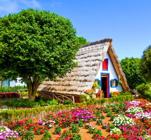 Traditionelles Strohdachhaus zwischen bunten Blumenbeeten und gr&uuml;nen B&auml;umen.