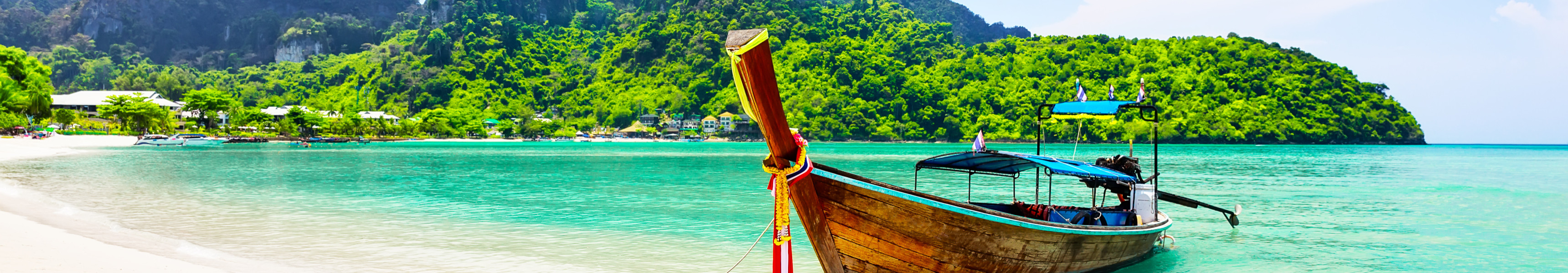 Traditionelles Longtail-Boot am wei&szlig;en Sandstrand mit t&uuml;rkisfarbenem Wasser und gr&uuml;nen Bergen auf Koh Phi Phi, Thailand