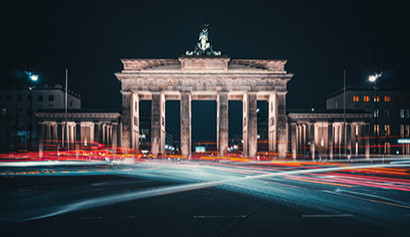 Das Brandenburger Tor in Berlin bei Nacht mit Lichtspuren vorbeifahrender Autos. 