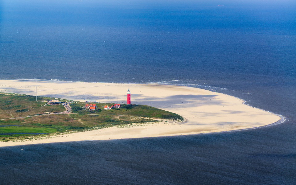 Luftaufnahme der niederl&auml;ndischen Insel Texel mit Sandstr&auml;nden, einem roten Leuchtturm und angrenzenden D&uuml;nenlandschaften inmitten der Nordsee.