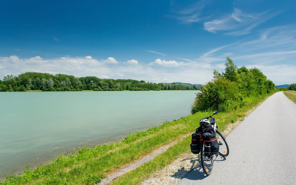 Fahrrad mit Gep&auml;ck auf dem Donauradweg mit Blick auf die Donau und umliegende gr&uuml;ne Landschaft