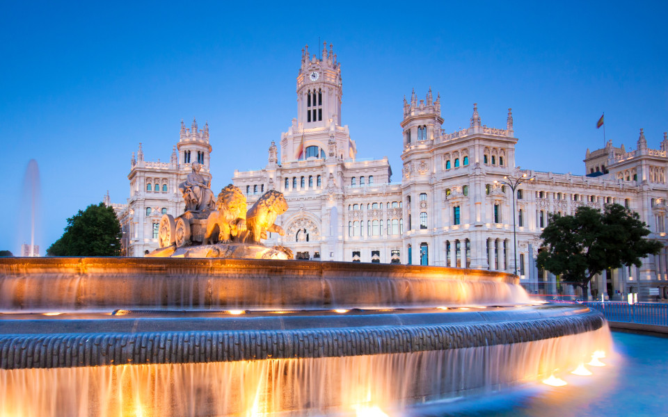 Der Cibeles-Brunnen in Madrid, beleuchtet im Abendlicht, vor dem beeindruckenden Palacio de Cibeles.